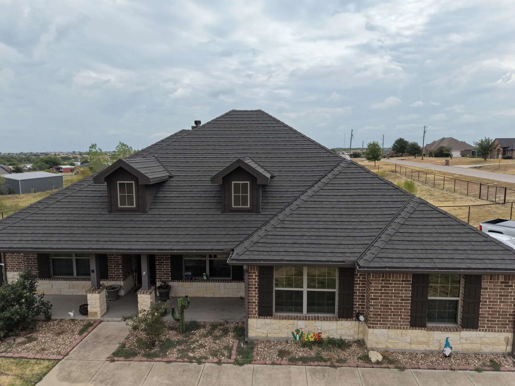 Weathered Wood Stormetal Shingle roof on a brick-and-stone home with dormers